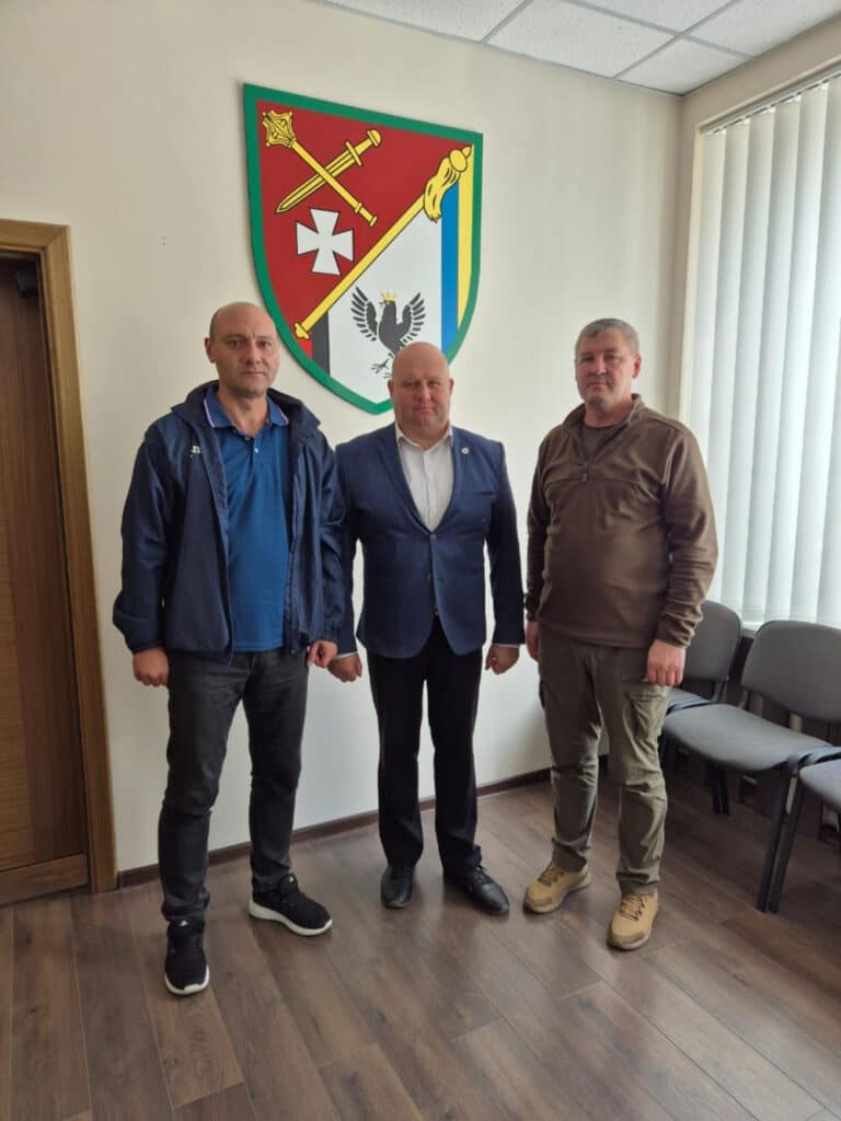 Троє чоловіків стоять перед гербом в кімнаті.