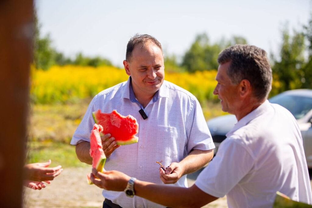 Чоловіки обговорюють та їдять кавун на природі.