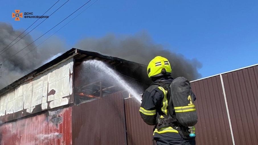 Пожежник гасить вогонь водяним струменем, дим над будівлею.