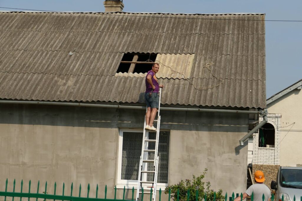 Чоловік ремонтує дах на драбині біля будинку.