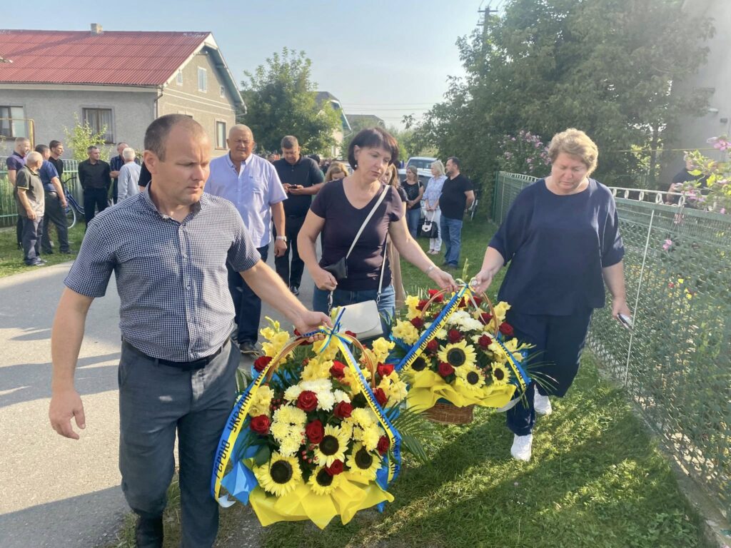 Люди несуть квіти на вулиці, група зібралась.
