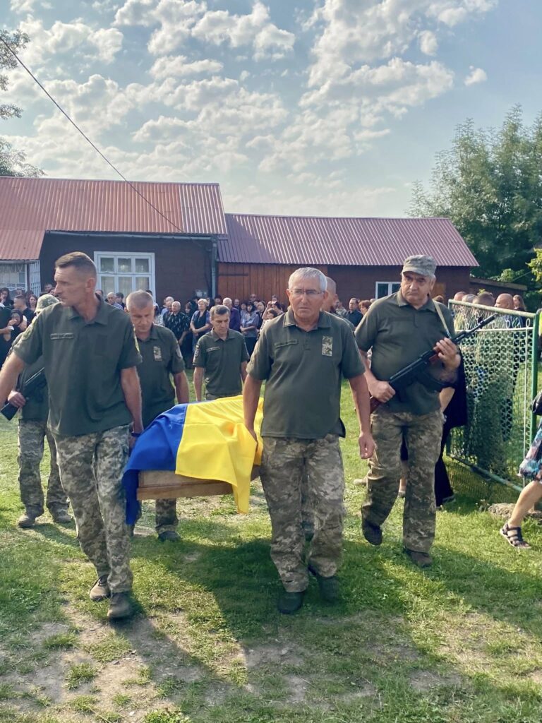 Військові несуть труну, накриту українським прапором.