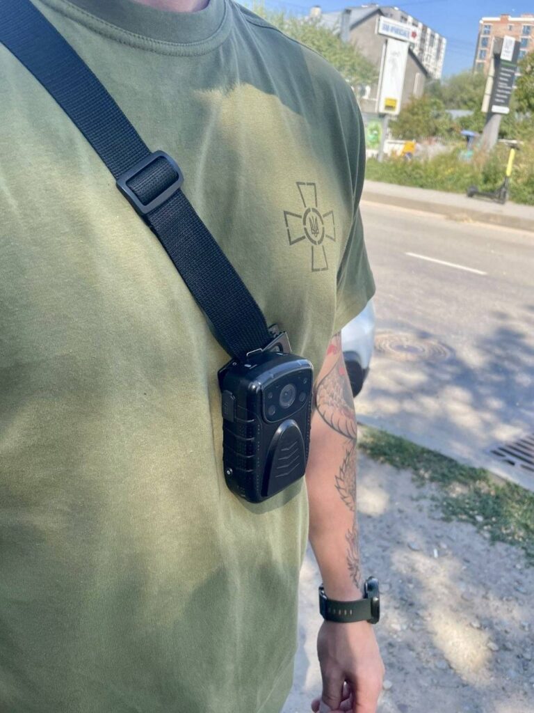 Чоловік у футболці з нагрудною камерою на ремені.
