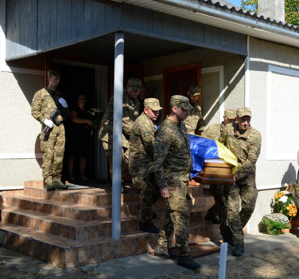 Військові несуть труну, покриту українським прапором.