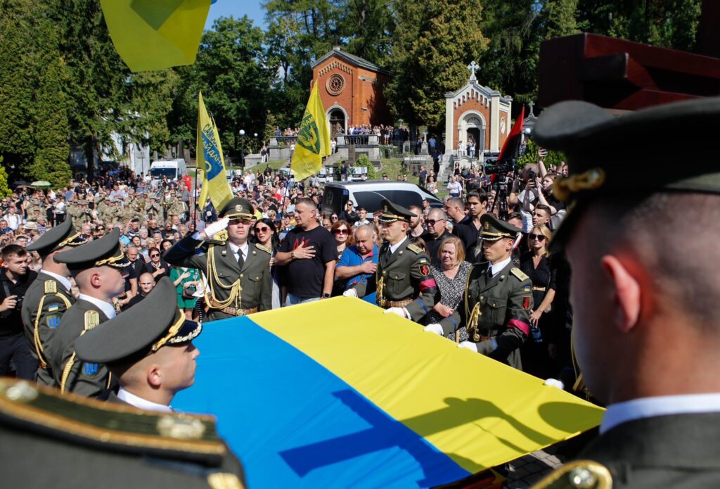 Військовий похорон з прапором України, натовп людей.