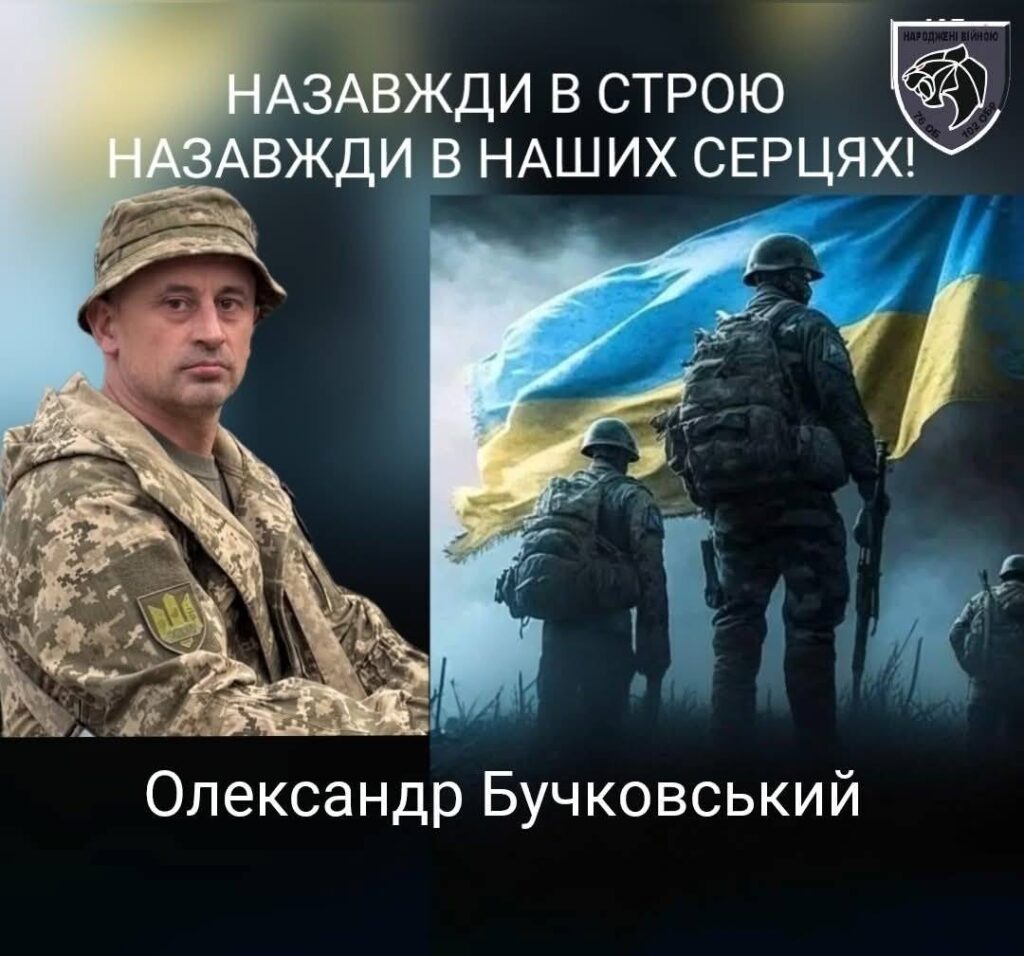 Військовий з прапором України на задньому плані.