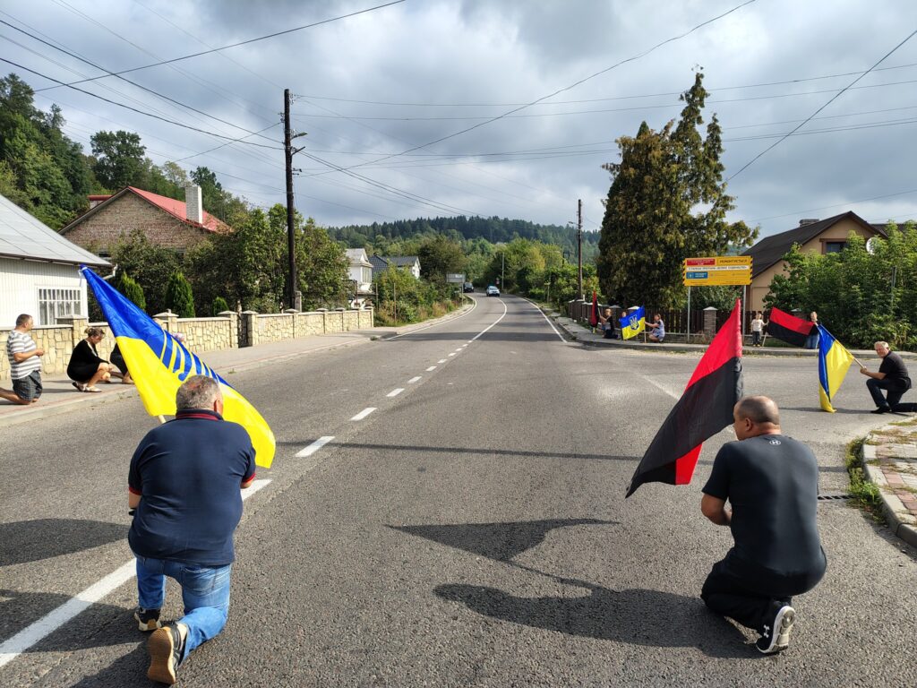 Люди з прапорами стоять на вулиці в селі.