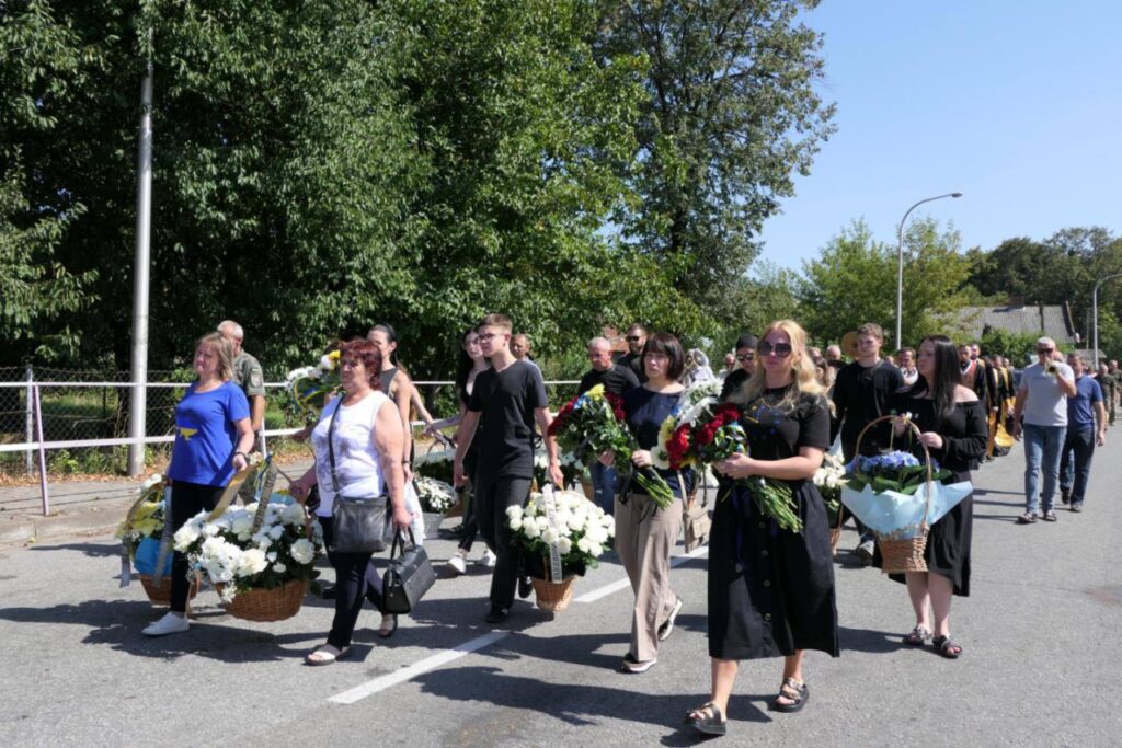 Люди в чорному несуть квіти у похоронній процесії.