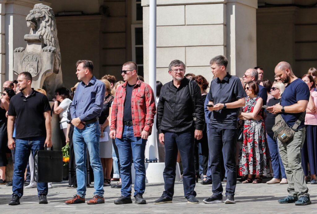 Люди стоять на площі біля статуї лева.