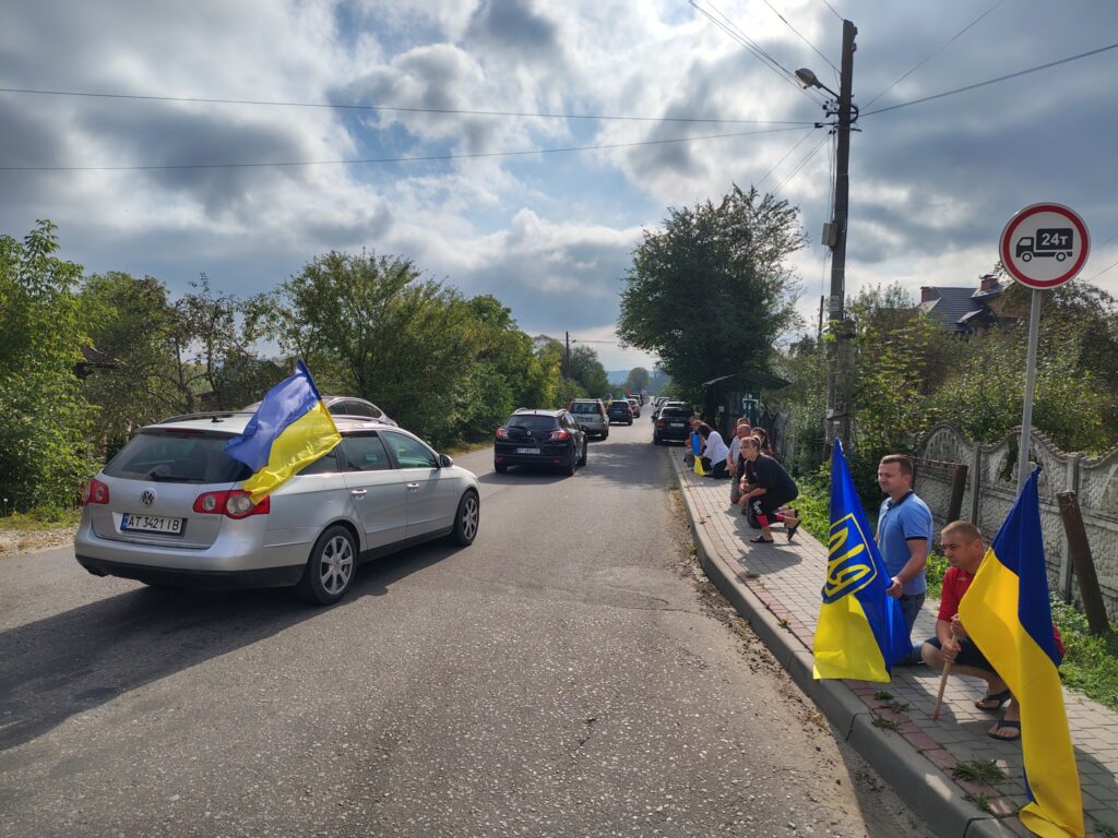 Автомобіль з українським прапором на дорозі, люди з прапорами