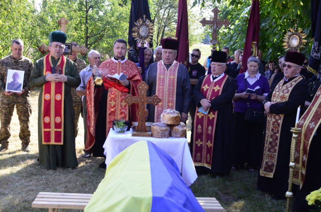 Поминальна церемонія з священиками біля труни з прапором.