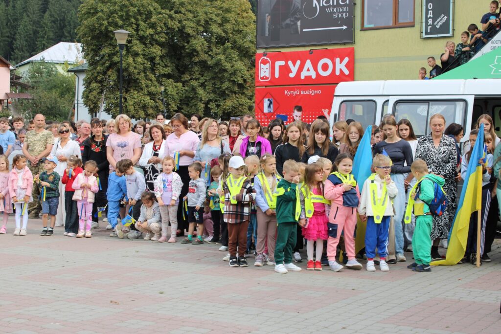 Діти та дорослі на урочистому заході на вулиці.
