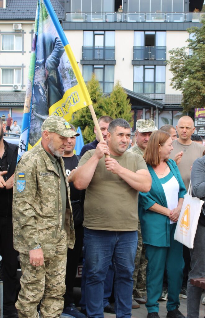 Люди з прапорами під час зібрання на вулиці.