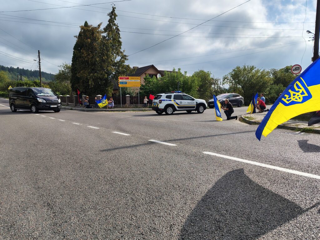 Люди з українськими прапорами біля дороги, поліція поруч.