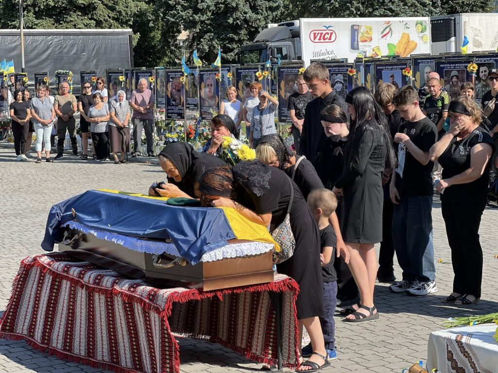 Люди прощаються з загиблим, обгорнутим українським прапором.