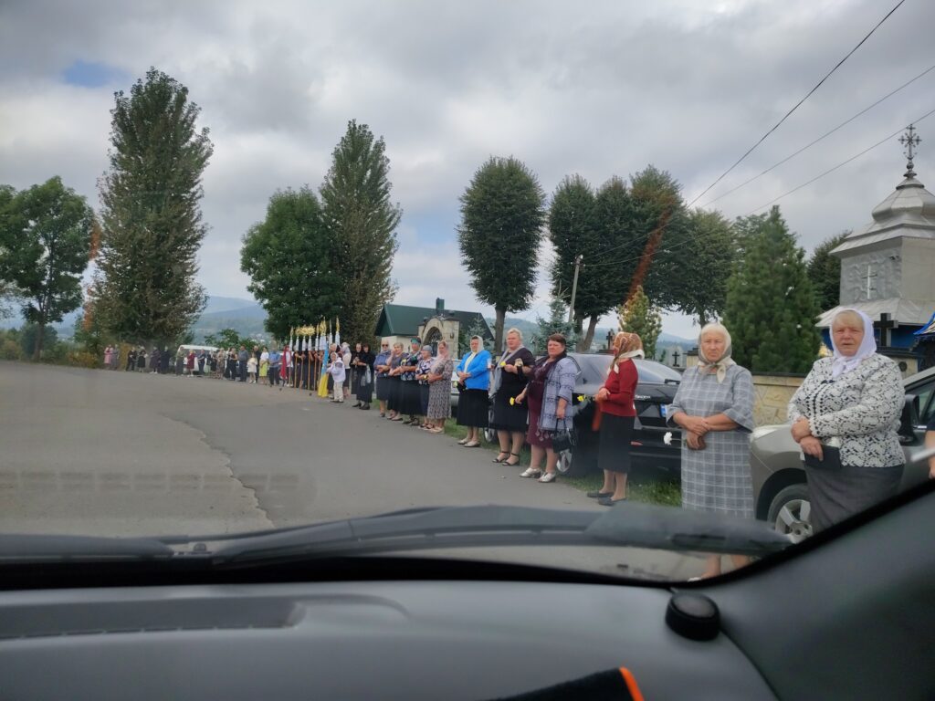 Люди стоять уздовж дороги біля церкви