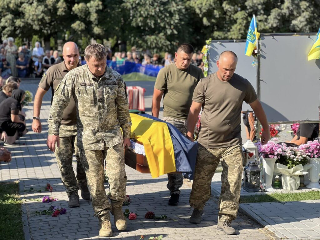 Військові несуть труну на похороні, прапори України