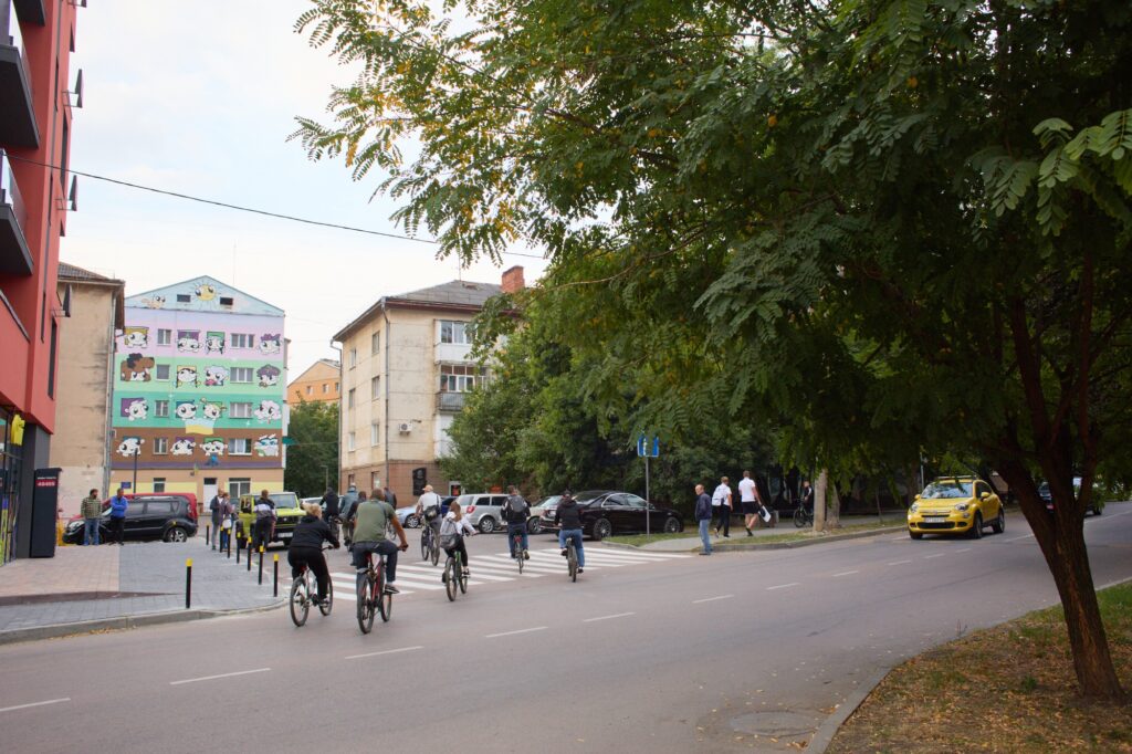 Люди на велосипедах біля розмальованої будівлі