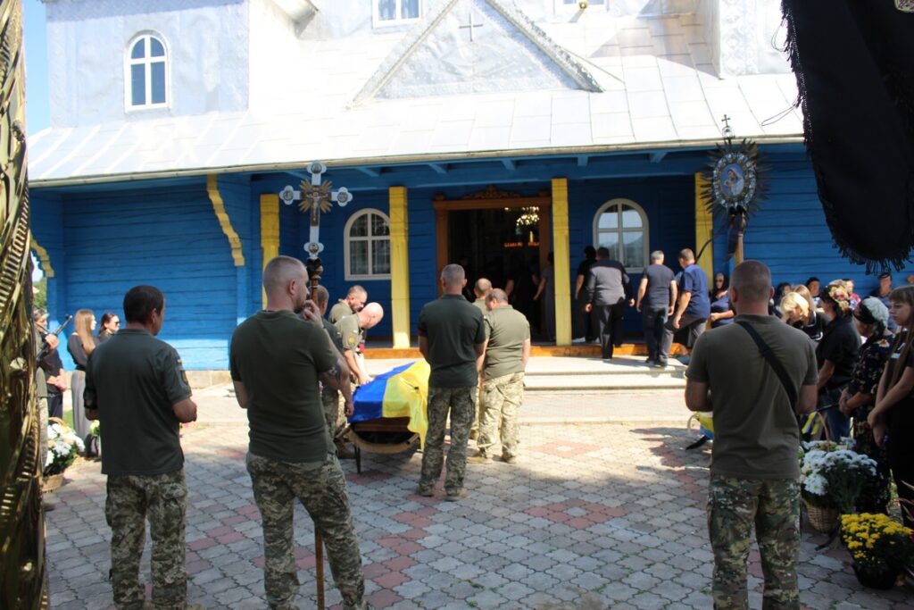 Похоронна церемонія біля синьо-жовтої церкви.
