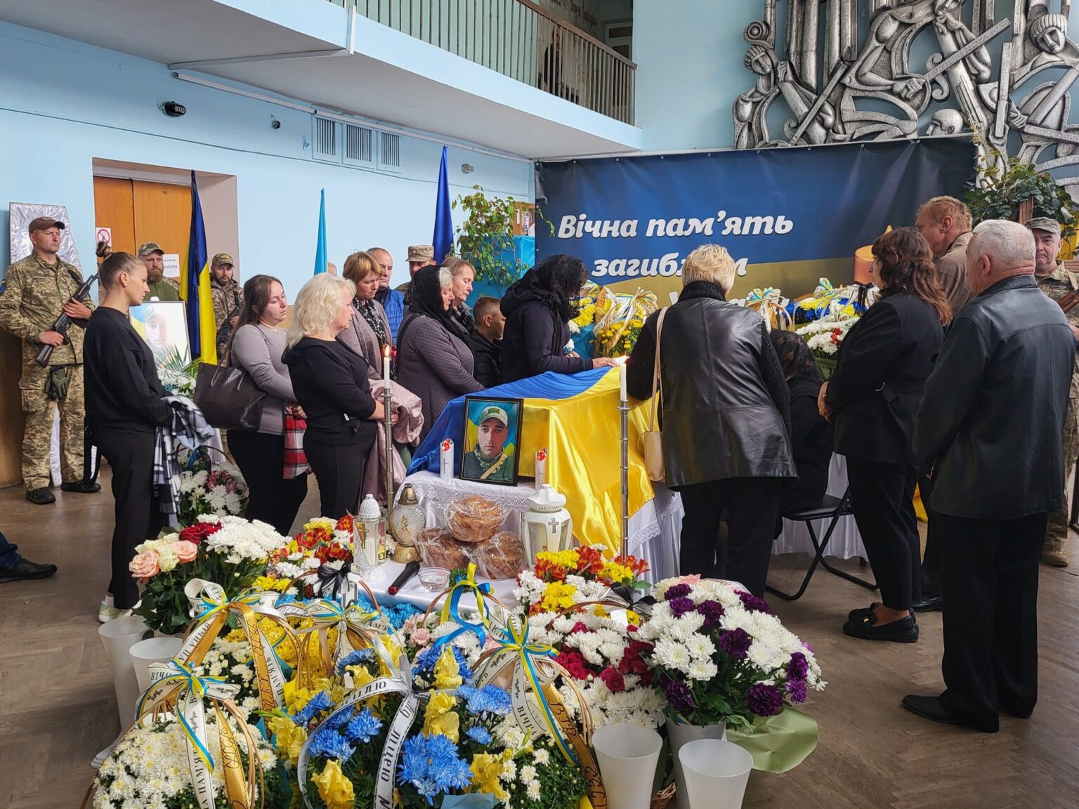 Люди вшановують загиблих військових у залі.