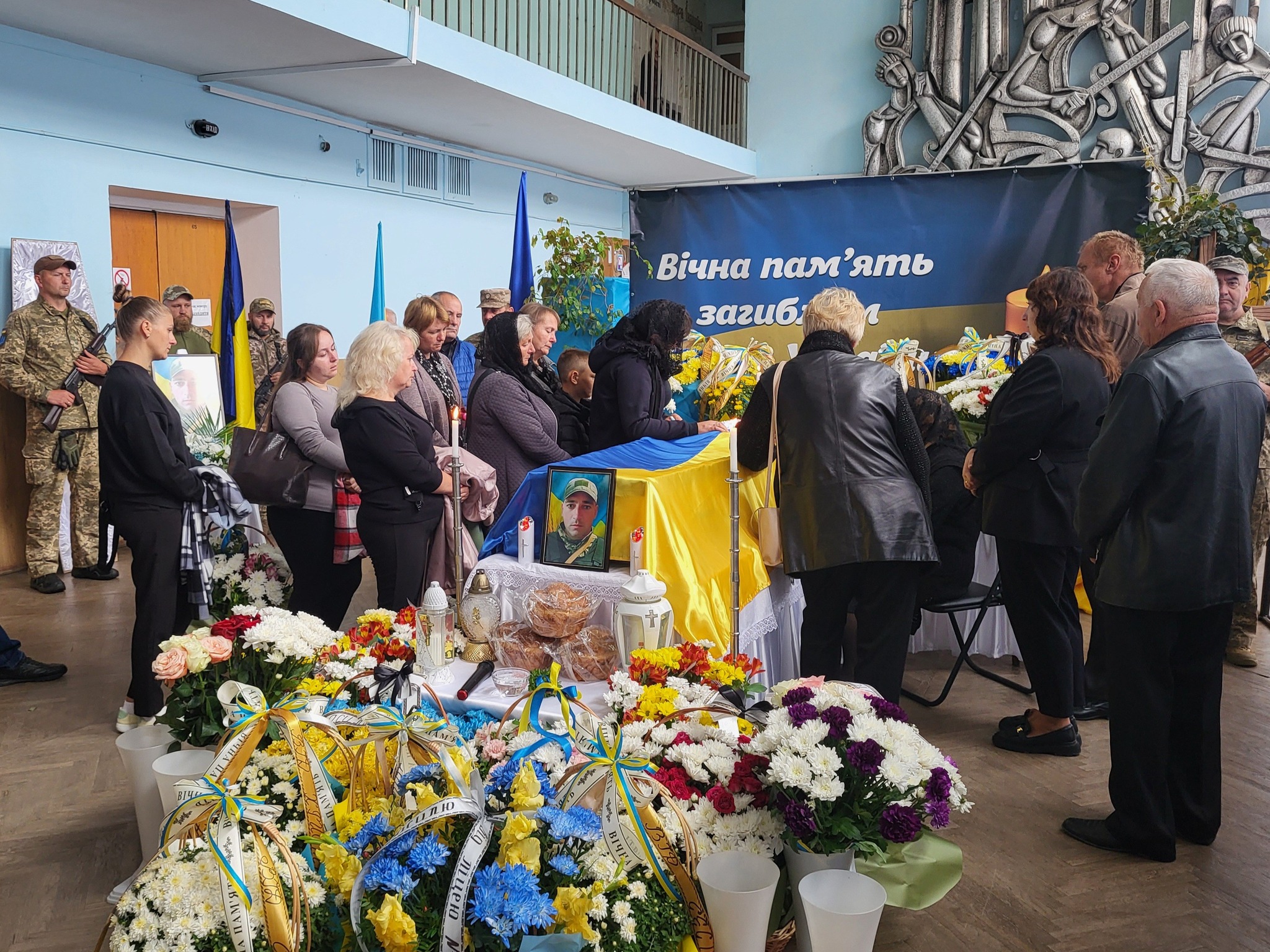Люди вшановують загиблих військових у залі.