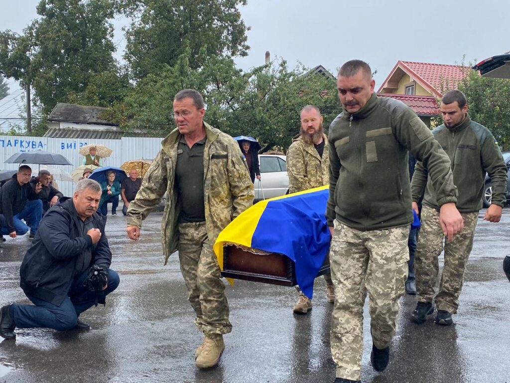 Військові несуть труну, накриту прапором України.
