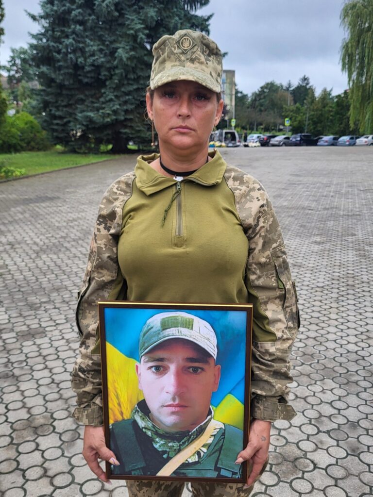 Жінка в формі з портретом військового.