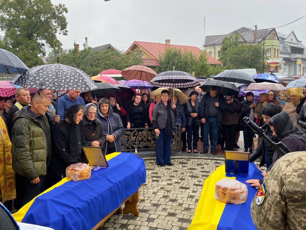 Люди під парасольками біля прапорів і хліба.