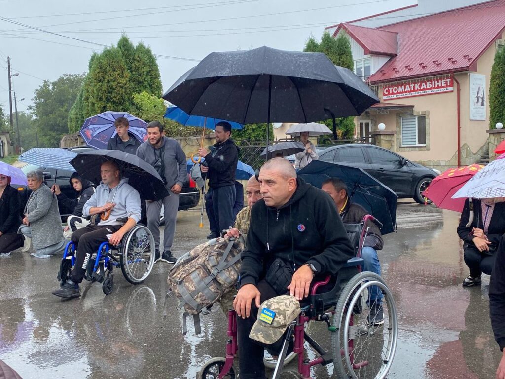 Люди під дощем із парасолями на вулиці.
