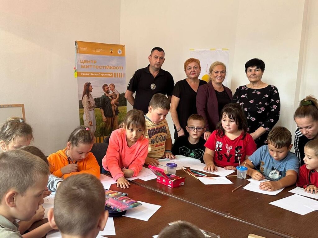 Діти на занятті, дорослі стоять позаду столу.