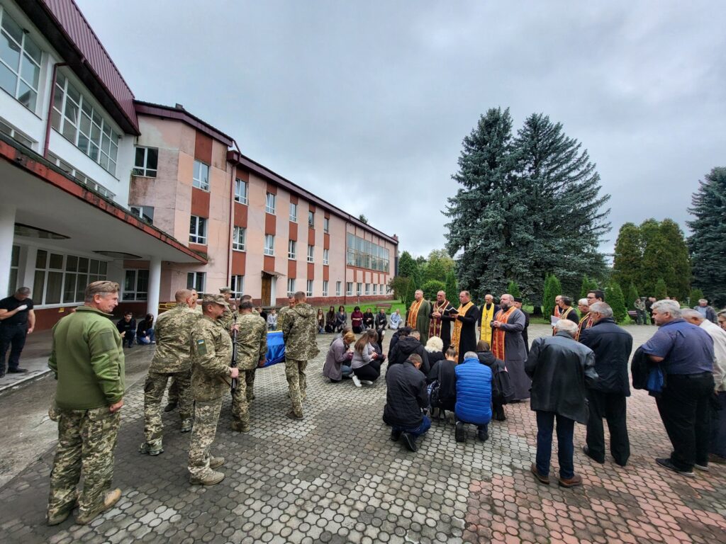 Військові церемонія біля будівлі, люди на колінах.