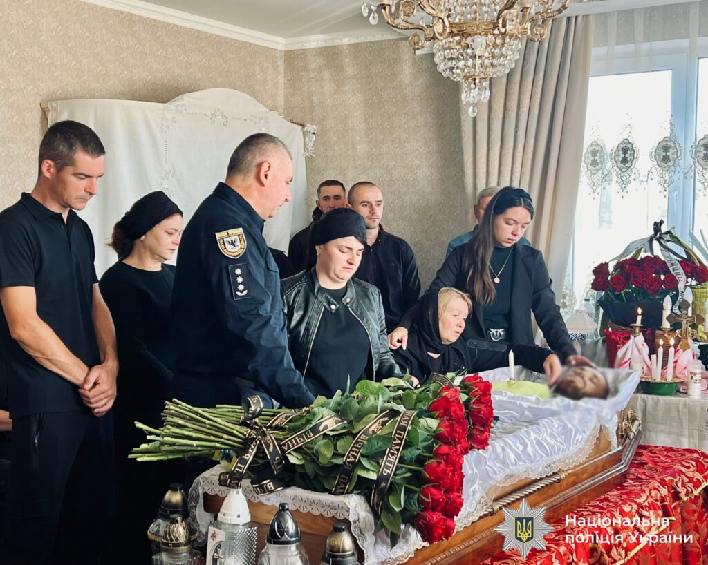 Люди сумують на похороні біля труни.