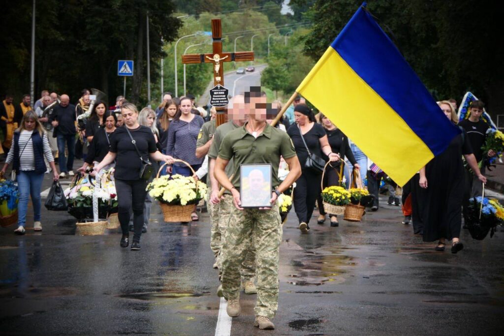 Люди несуть прапор, портрет і квіти на церемонії.