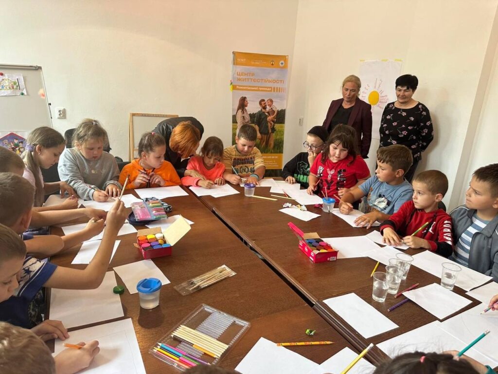 Діти малюють за столом під наглядом дорослих.
