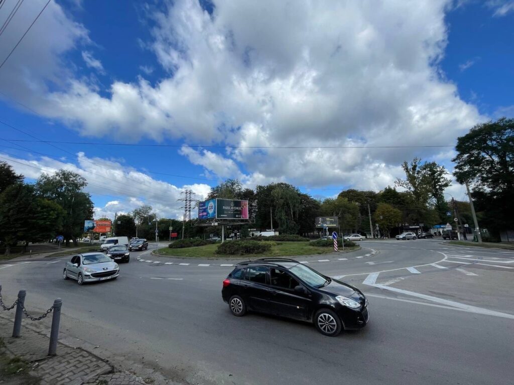 Круговий рух з автомобілями і рекламними щитами.