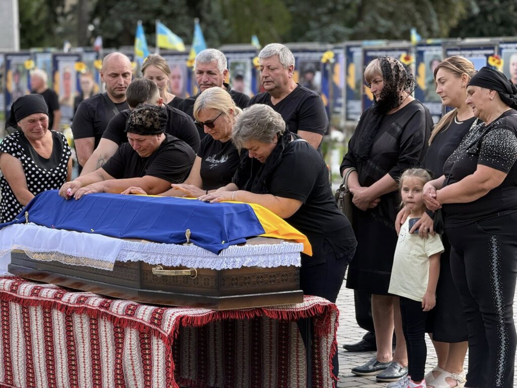 Люди прощаються з померлим, накритим українським прапором.