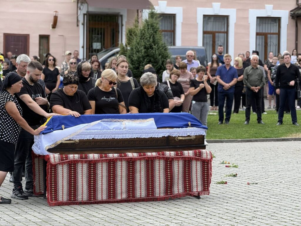 Люди прощаються біля труни на вулиці.