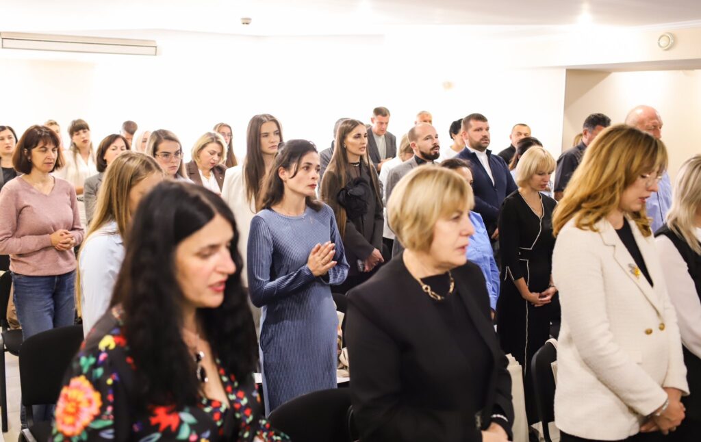 Люди стоять на зустрічі або заході у приміщенні.