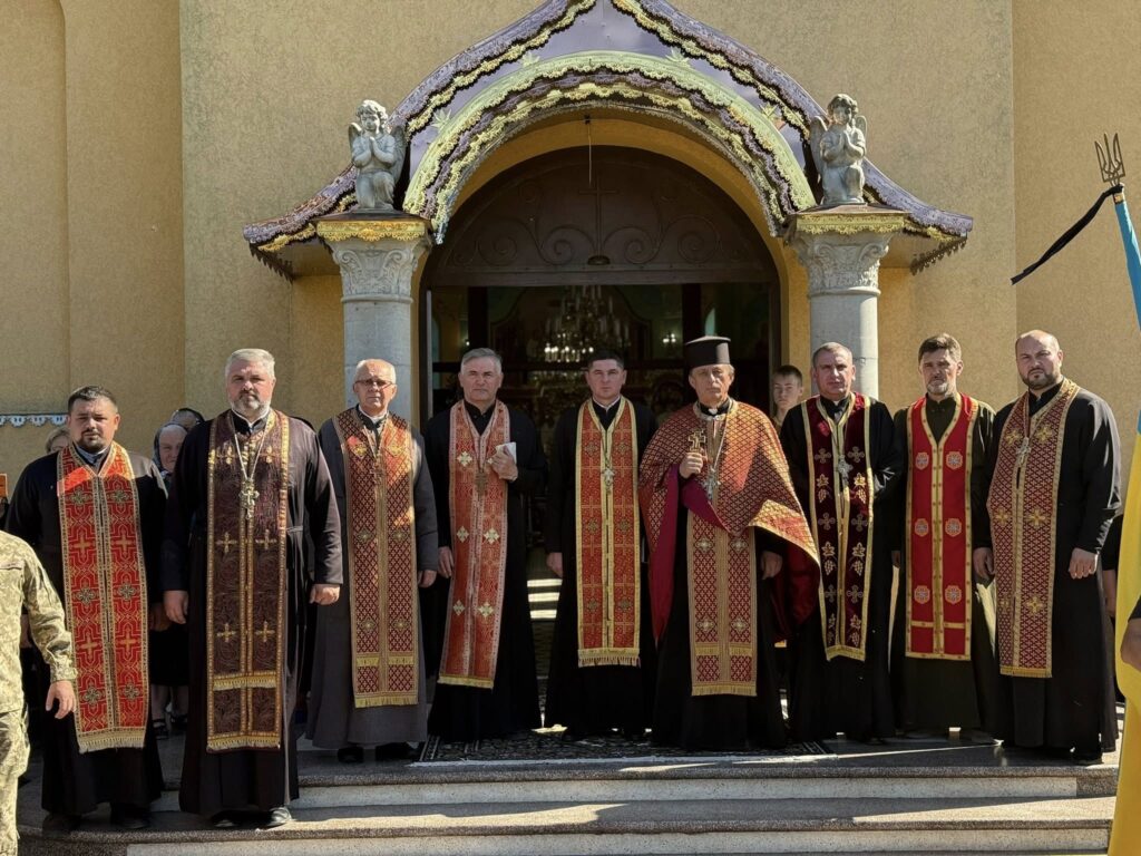 Духовенство біля церкви з українським прапором