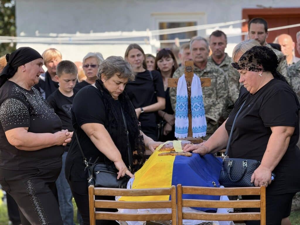 Люди скорбіють біля труни під прапором України.