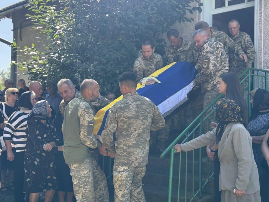 Військові несуть труну, вкрита українським прапором.