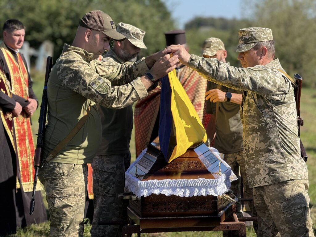 Українські військові накривають труну на похороні.