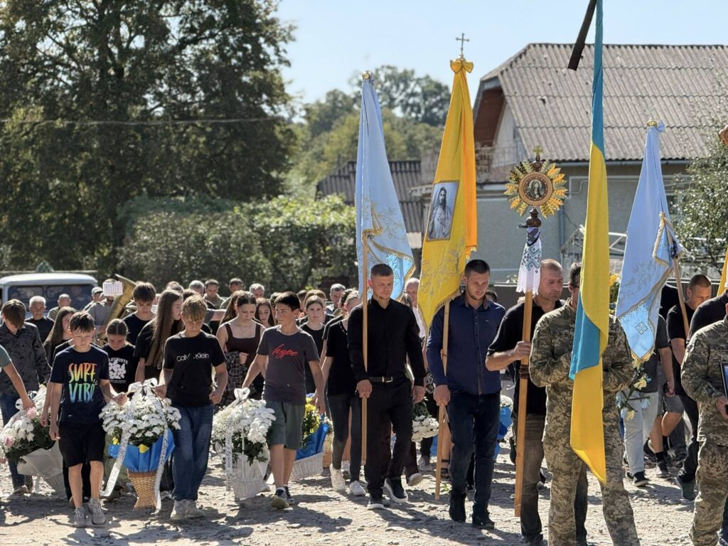 Процесія з прапорами під час похорону на вулиці.