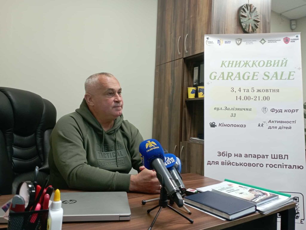 Чоловік на пресконференції оголошує книжковий розпродаж.