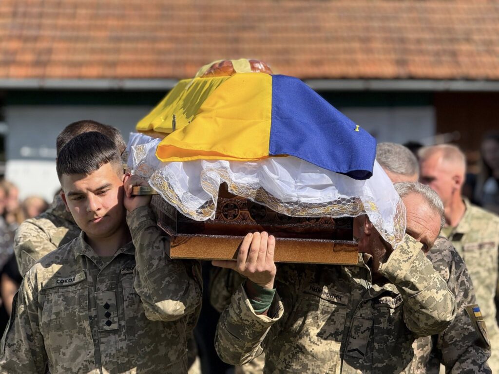 Військові несуть труну, вкрита прапором України.