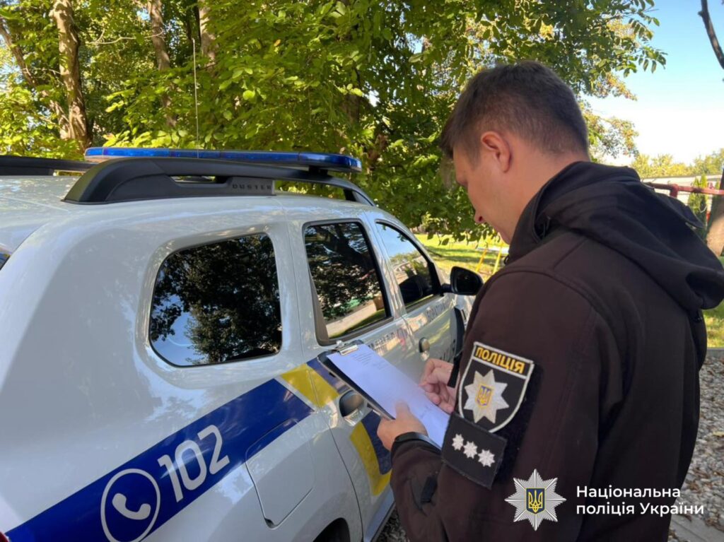 Поліцейський поруч з патрульним автомобілем, пише звіт.