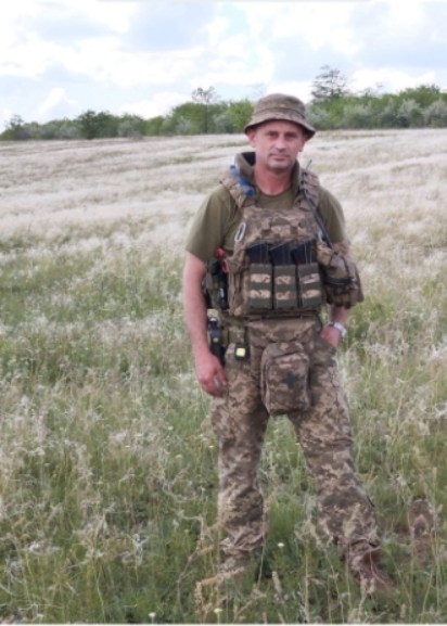 Солдат в полі у військовій формі тримає автомат.