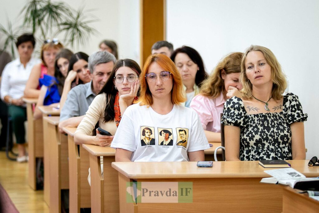 Люди сидять за дерев'яними столами в аудиторії.