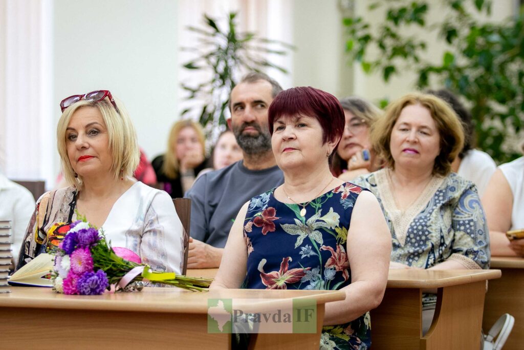 Люди на заході у залі з квітами на столі.
