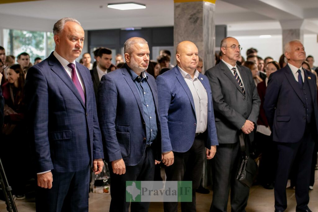 Чоловіки в костюмах на публічному заході, натовп ззаду.